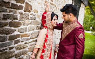 indian couple wearing traditional wedding outfits posing together in a park next to the stone wall