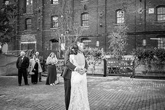 black and white photo of bride and groom hugging in front of the family in distillery